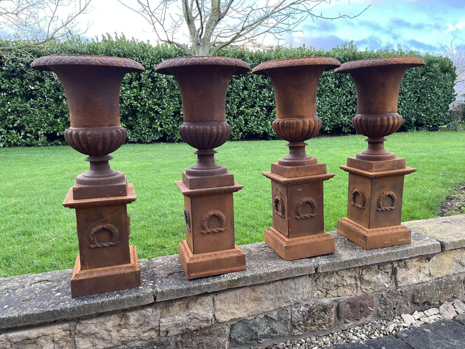 Set of four cast iron urns on plinths