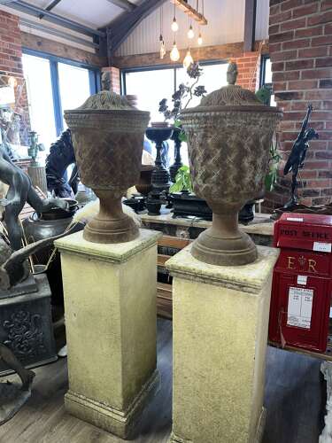 Pair of antique cast iron urns on stone plinths.