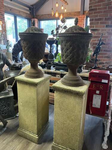 Pair of antique cast iron urns on stone plinths.